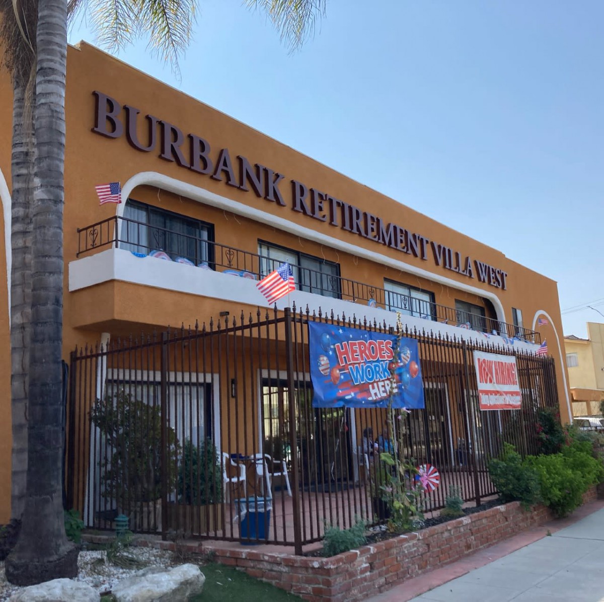 An outdoor view of a restaurant named Burbank Pizzeria & Restaurant with palm trees and banners displayed on the building.