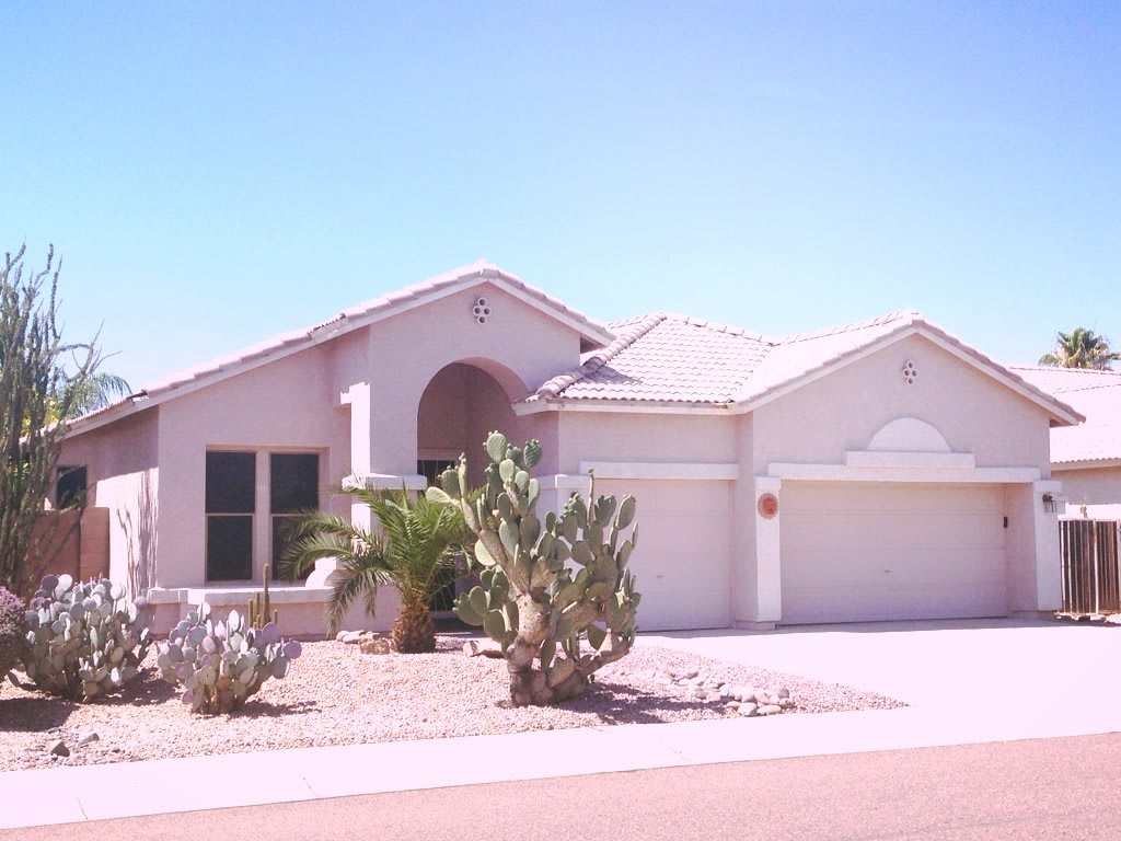 A single-story suburban house with a desert landscape and cactus in the front yard.