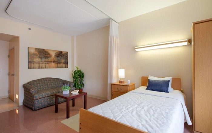A cozy bedroom with a single bed, sofa, and warm lighting.