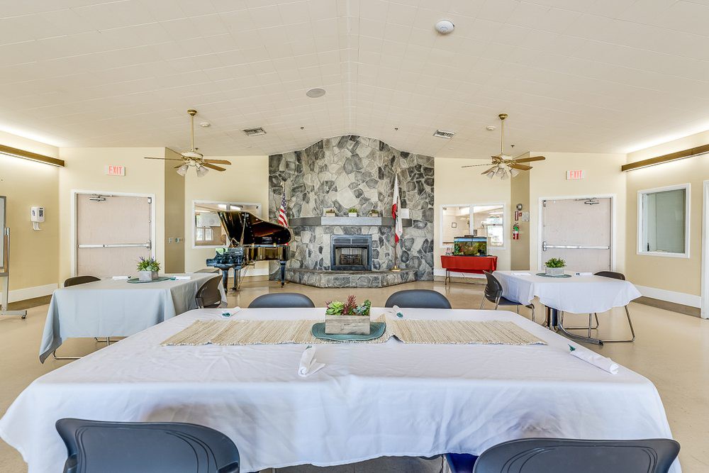 A spacious dining area featuring neatly arranged tables and chairs, with a grand piano and a decorative fireplace as focal points.