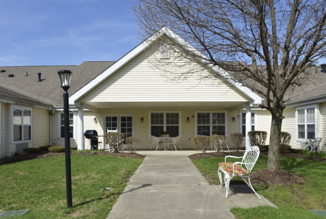 A small house with a porch, featuring chairs and a pathway leading up to it.