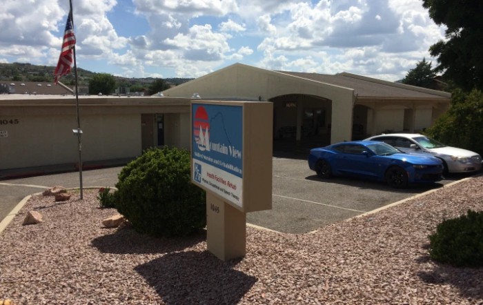 A building with a sign and a parked car under a cloudy sky.