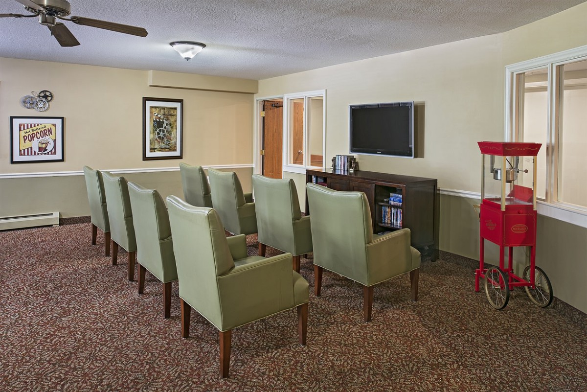 A small theater room with a row of green chairs facing a television.