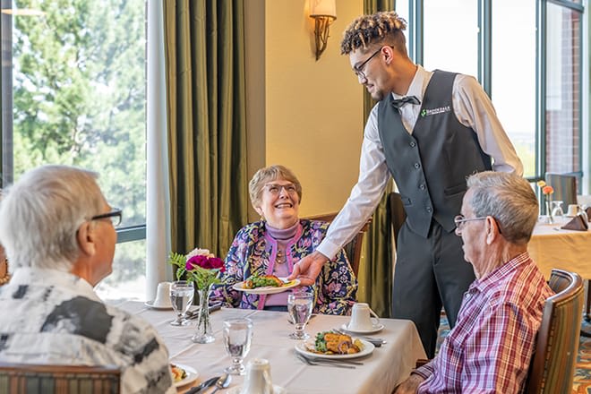 A waiter serves a meal to elderly patrons at a restaurant.