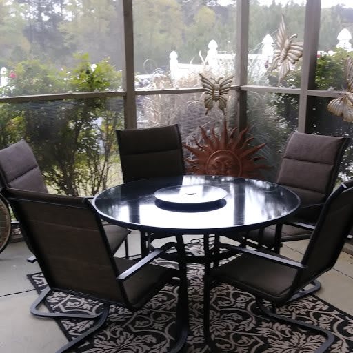 A cozy screened porch with a round table and four chairs surrounded by potted plants.