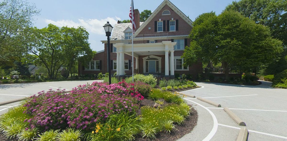 A large house with a well-maintained garden and an American flag on a sunny day.
