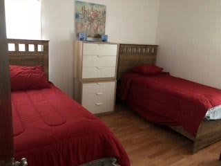 A bedroom with two beds covered in red bedding, a dresser between them, and a wooden floor.