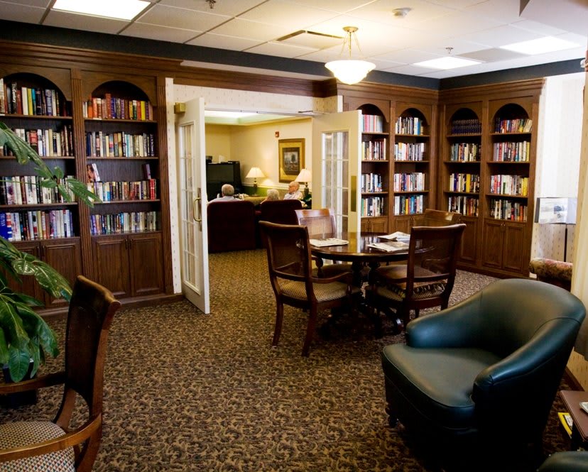 A cozy library room with bookshelves, a table, and chairs arranged for reading.