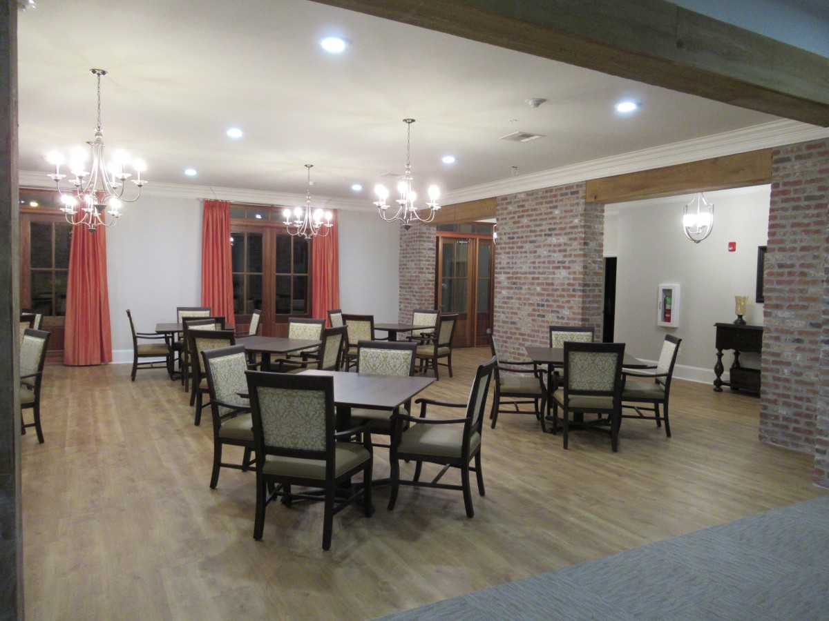 A spacious dining area with tables and chairs, featuring chandeliers and wooden flooring.