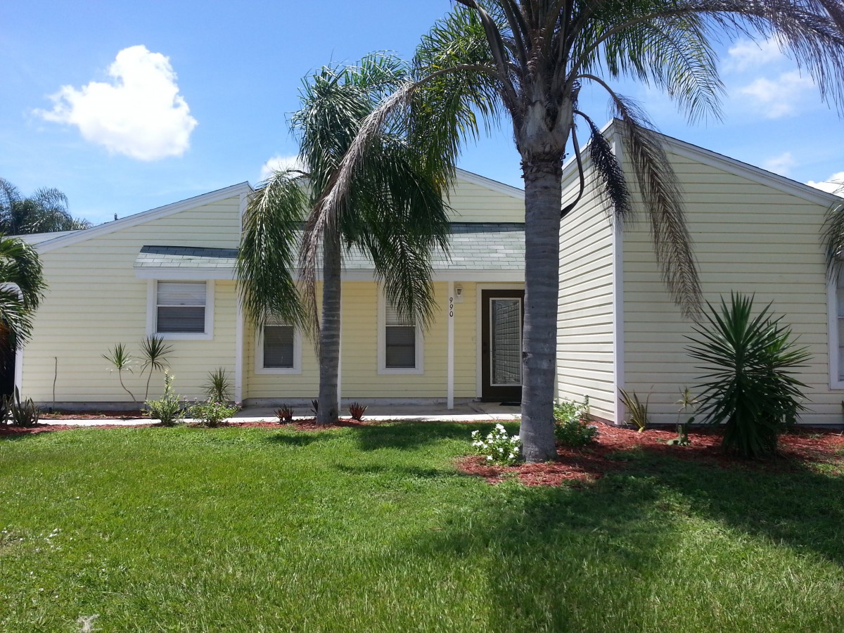 A suburban house with palm trees and a well-maintained lawn under a sunny sky.