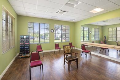 A spacious room with green walls, windows, and chairs arranged in a circle on hardwood flooring.