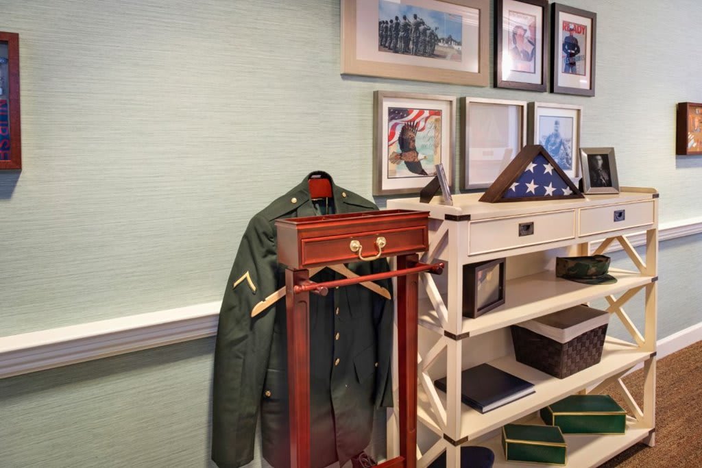 A military jacket on a wooden stand, with framed photographs and a folded flag in a display case.