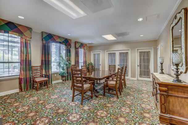 A well-lit conference room with a large table and chairs, surrounded by windows with decorative curtains and a floral patterned carpet.