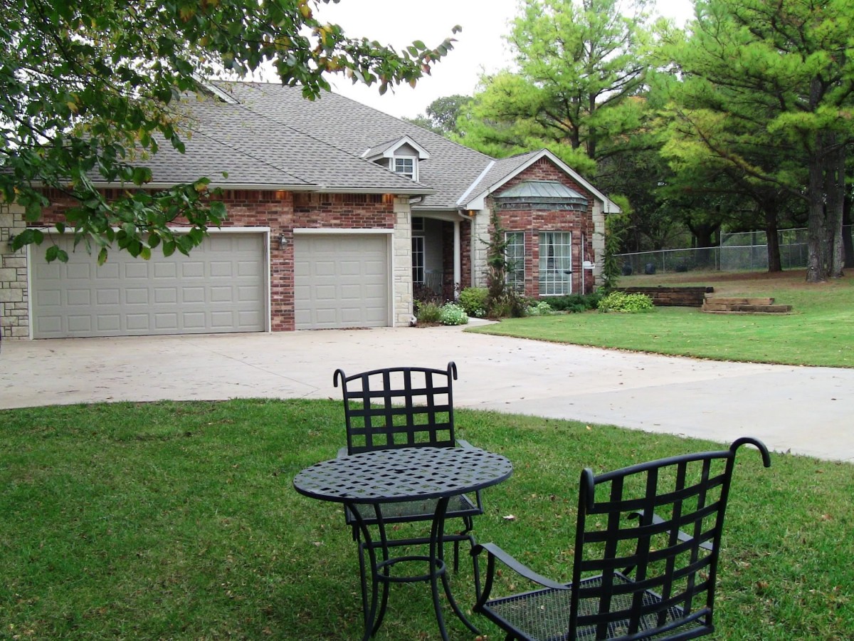 A suburban house with a driveway, surrounded by a green yard featuring a patio table and chairs.