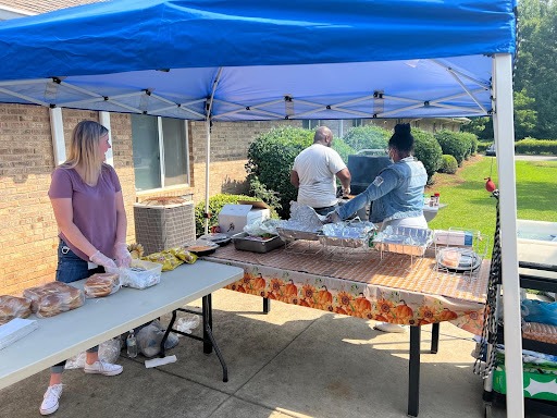 A lively outdoor barbecue gathering with food preparation under a blue tent.
