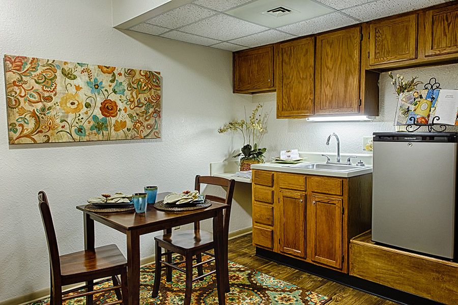 A small kitchen and dining area featuring wooden cabinets, a table with chairs, decorative wall art, and a cozy atmosphere.