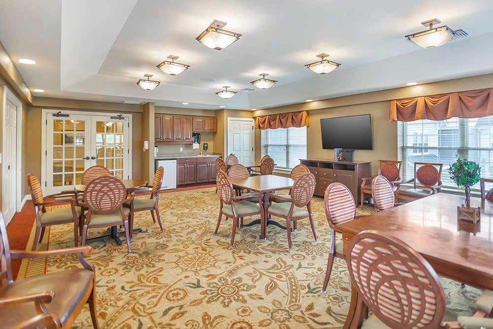A spacious dining area with multiple tables and chairs, a large television, and a kitchenette in the background.