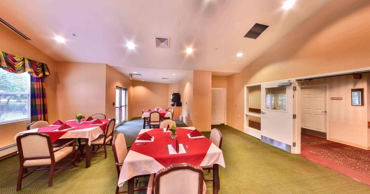 A cozy restaurant dining room with tables set for service, featuring red tablecloths and elegant decor.