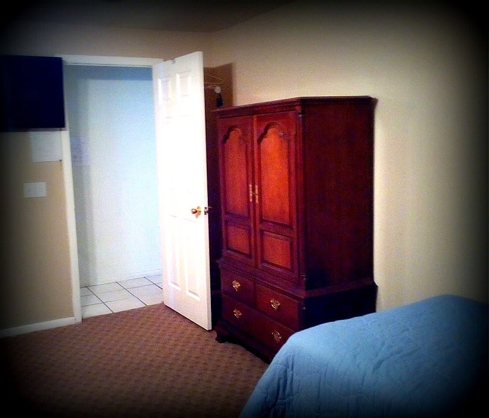 A cozy bedroom featuring a wooden armoire and an open doorway.