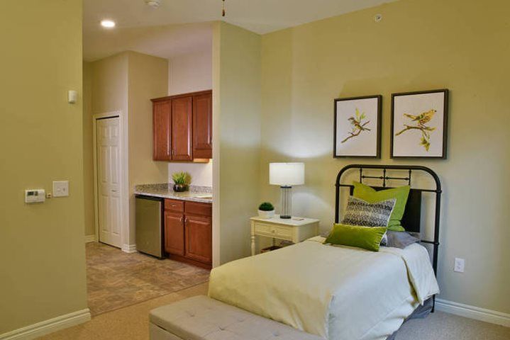 A modern and cozy bedroom with a neatly made bed, stylish decor, and a small kitchenette area.