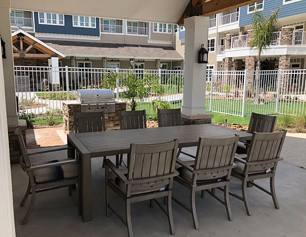 An outdoor patio area featuring a large dining table with chairs, situated near a garden and building.