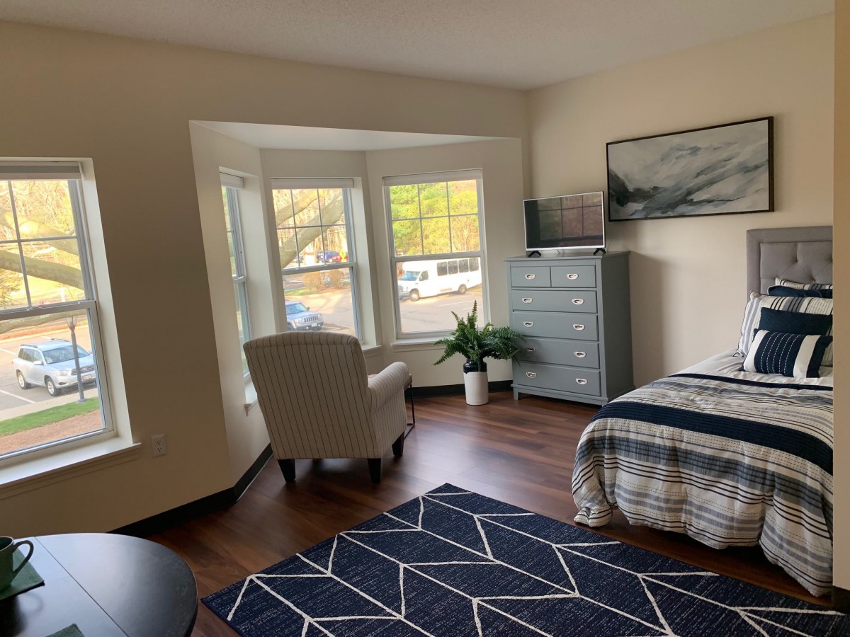A cozy bedroom with a large window, comfortable chair, and a neatly made bed.