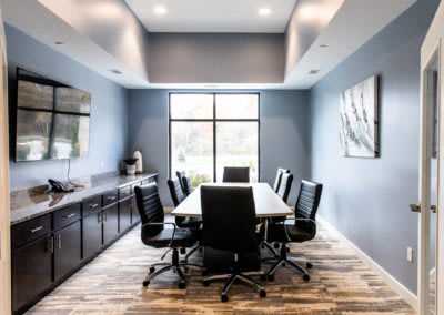 A modern conference room with a large table and leather chairs, illuminated by natural light from a window.