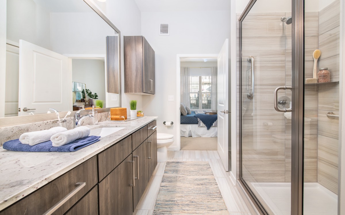 A modern bathroom with wood cabinetry, a large mirror, and a spacious shower.