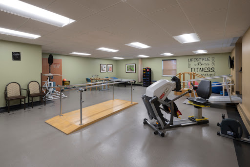 A spacious fitness room equipped for rehabilitation and exercise, featuring various machines and a ballet bar.