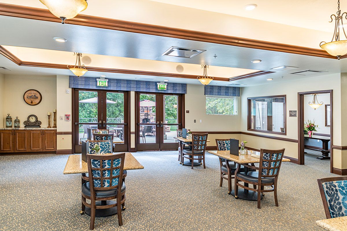 A spacious dining area with tables and chairs, featuring large windows and doors for natural light.