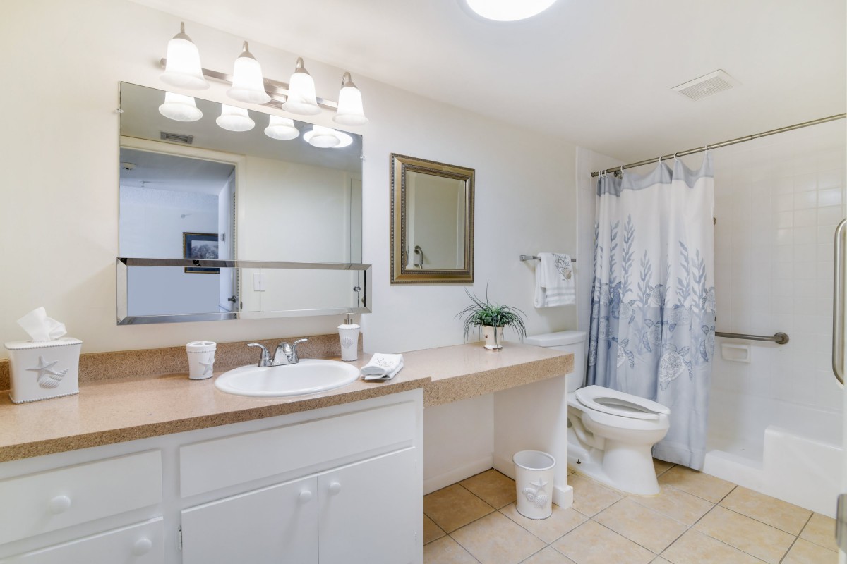 A well-lit bathroom with a large mirror, spacious countertop, sink, and shower area.