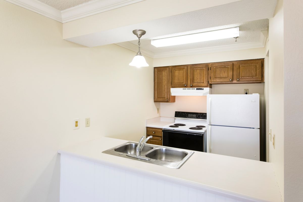 A compact apartment kitchen featuring wooden cabinets and basic appliances.