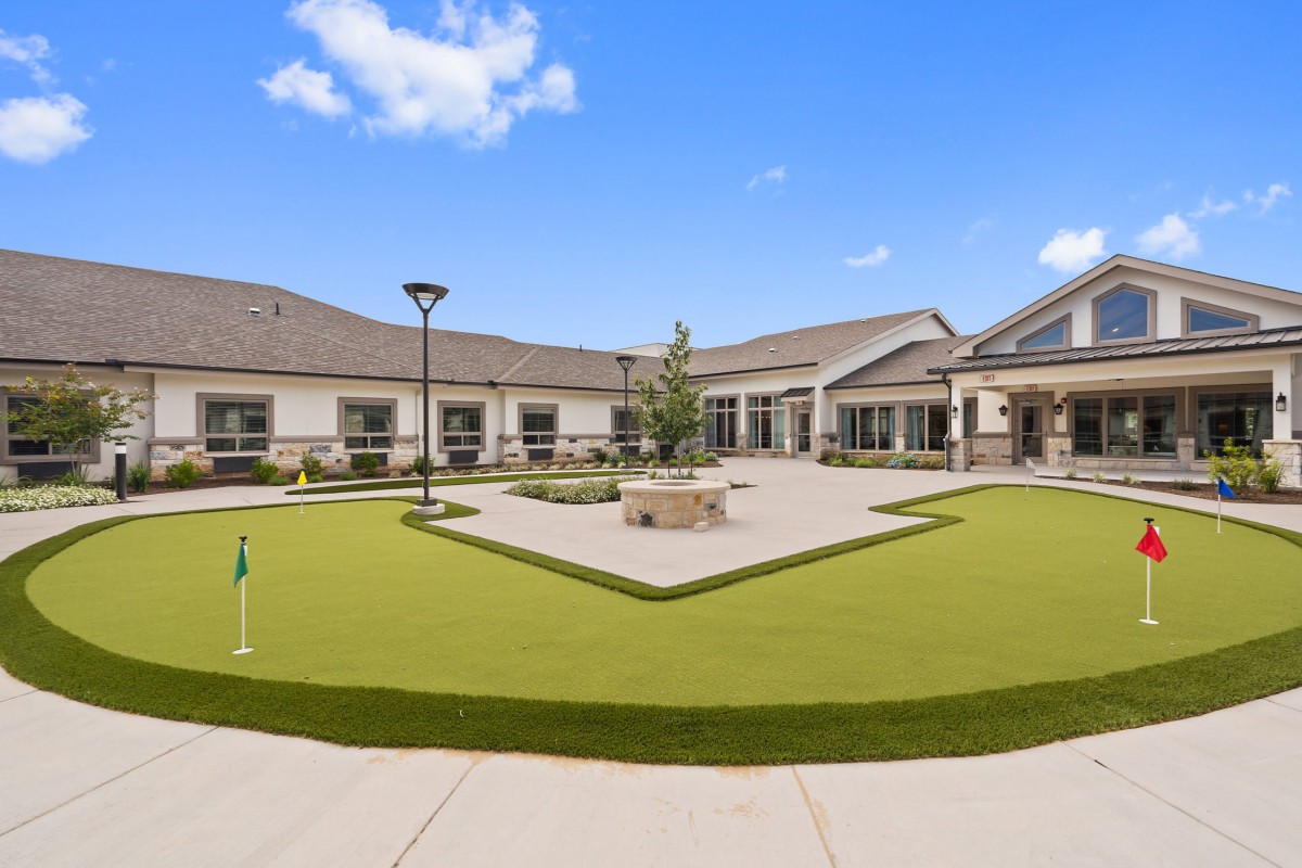 A modern building with a landscaped courtyard featuring a lawn and pathways under a clear blue sky.