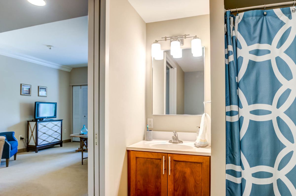 A modern bathroom featuring a wooden cabinet with a sink, a mirror above, and a blue patterned shower curtain.