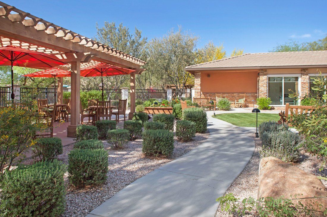 A well-designed outdoor space featuring a patio with tables and chairs, surrounded by lush landscaping under a clear blue sky.
