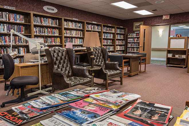 A cozy library reading area with bookshelves, magazines, and comfortable chairs.