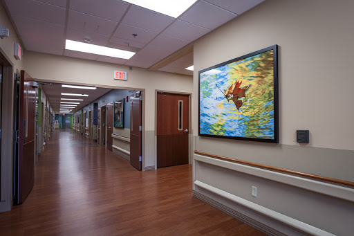 A brightly lit hospital corridor featuring a vibrant painting on the wall.