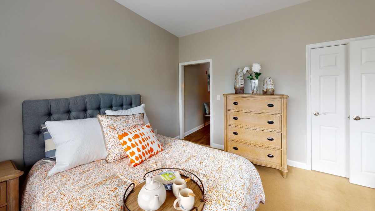 A cozy bedroom with a neatly made bed and a wooden chest of drawers, showcasing simple and elegant decor.