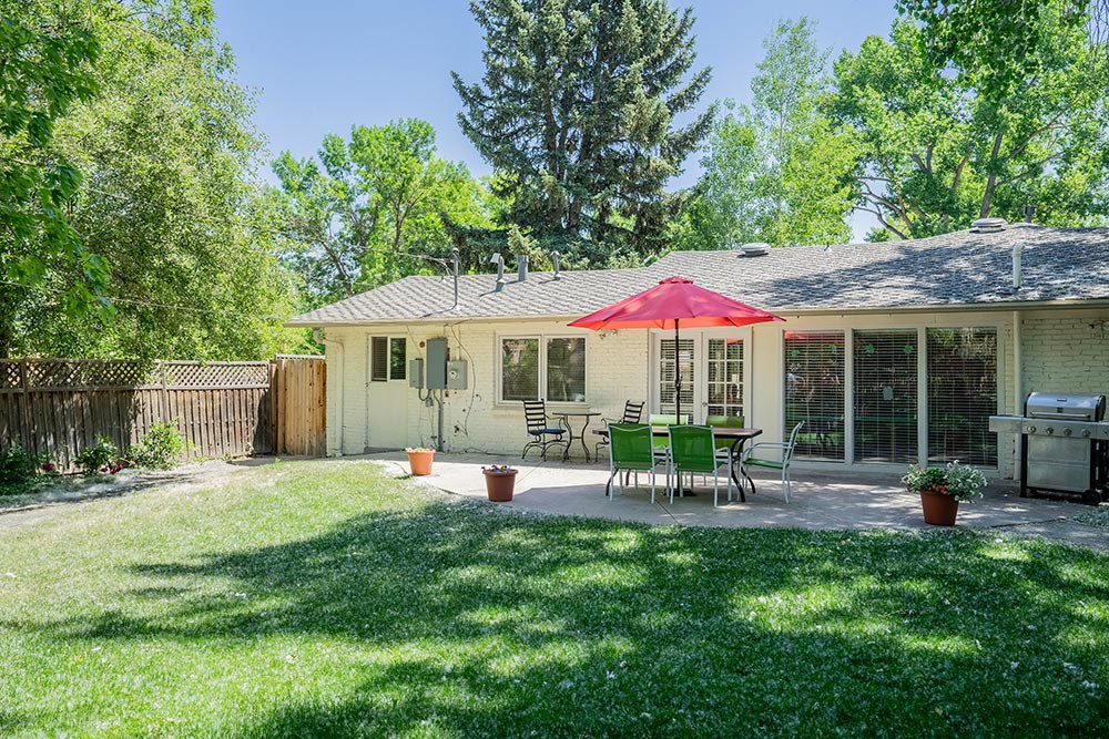 A cozy backyard with a patio set and vibrant umbrella surrounded by lush greenery.
