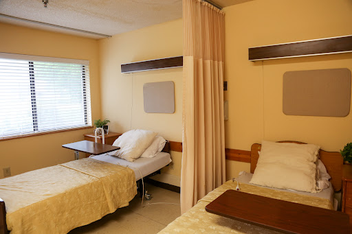A well-lit hospital patient room featuring two beds separated by a curtain.