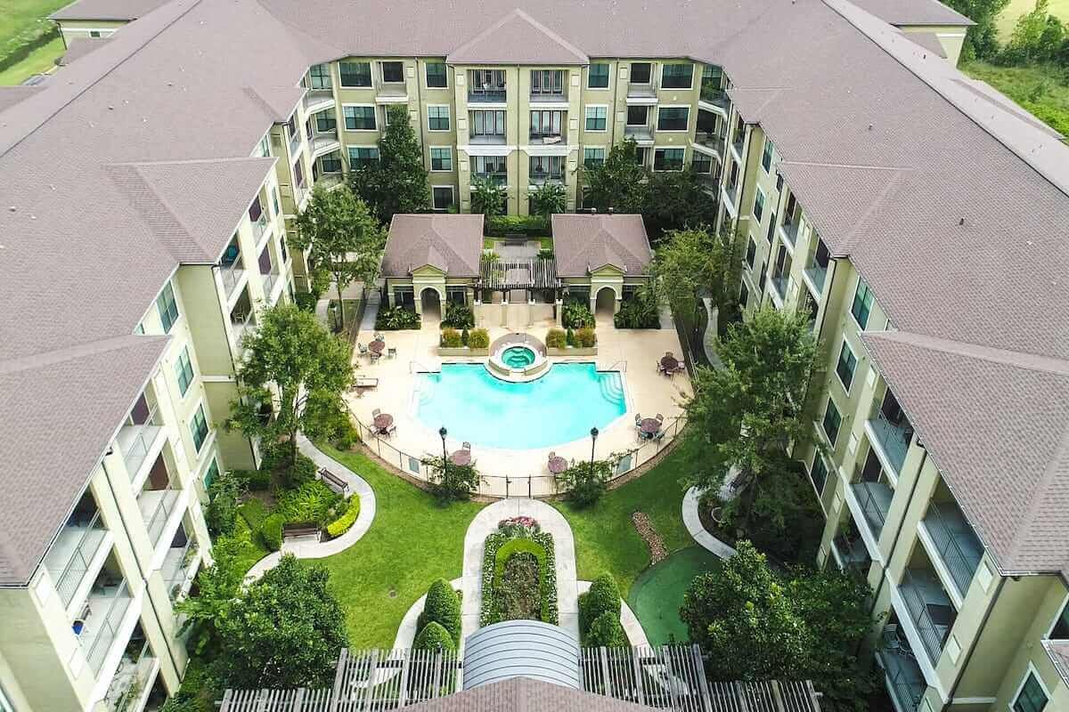 Aerial view of a modern apartment complex featuring a central swimming pool and well-maintained landscaping.