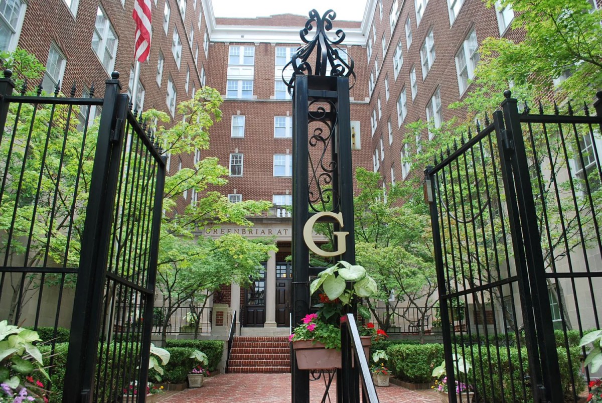 An entrance gate with a prominent 'G' leading to a brick building, surrounded by greenery.