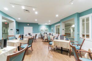 A modern dining room with neatly arranged tables and chairs, featuring light blue walls and wooden flooring.