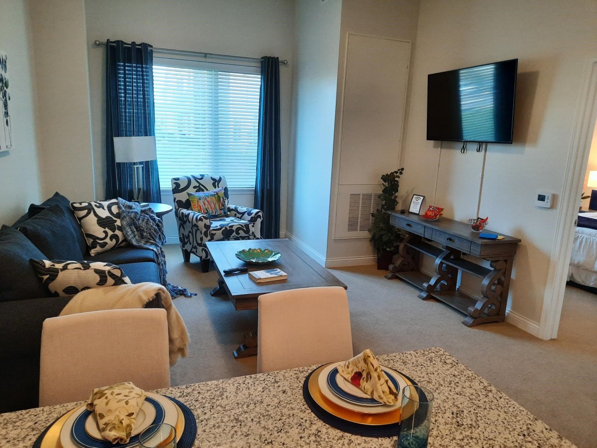 A stylish living room with modern decor, featuring a wall-mounted TV and cozy seating arrangements near a dining area.