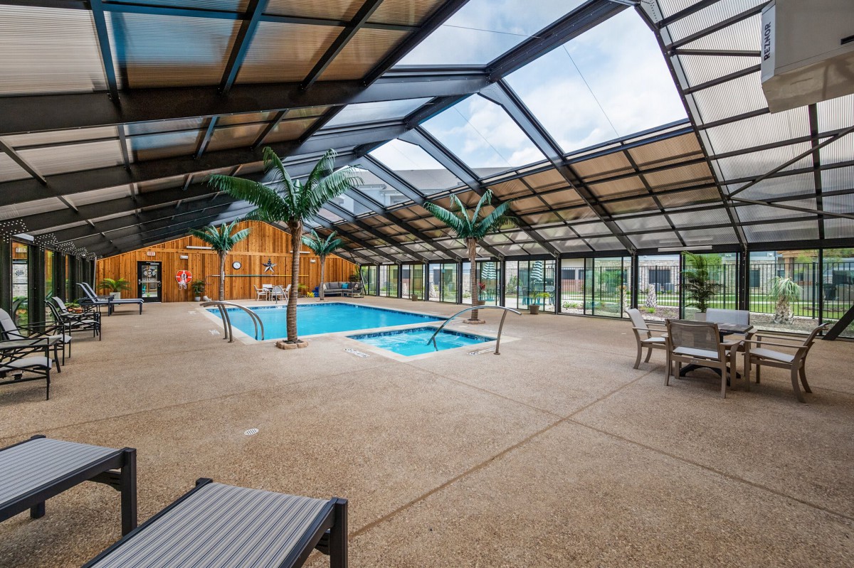 An indoor swimming pool area with a glass roof, featuring lounge chairs and palm trees.