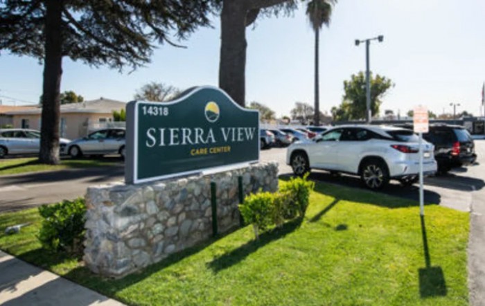 The image shows the sign for Sierra View apartments located next to a parking lot filled with cars on a sunny day.
