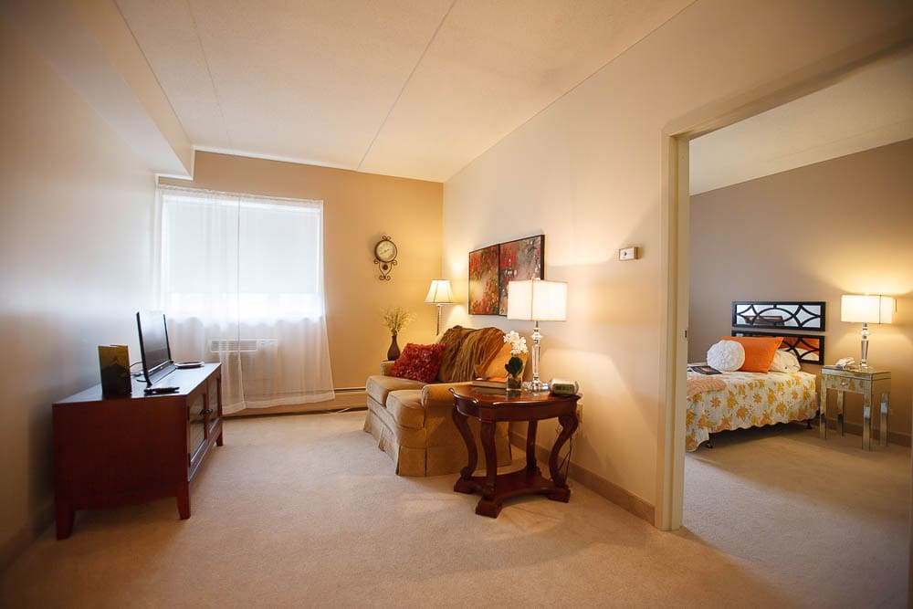 A cozy apartment living room with a sofa, lamps, and a view into the bedroom.