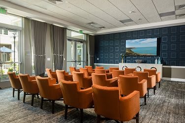 A well-equipped conference room with orange chairs facing a presentation screen.