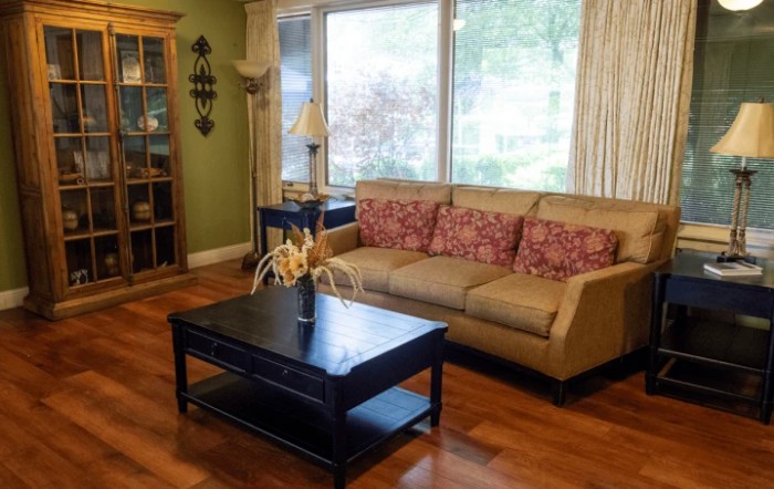 A cozy living room with a sofa and coffee table, featuring large windows and a hardwood floor.