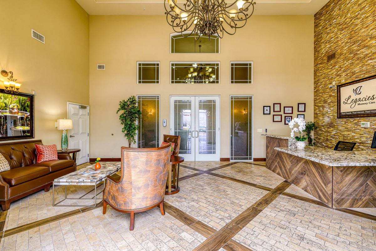 A spacious lobby with elegant decor, featuring a chandelier, comfortable seating area, reception desk, and indoor plants.